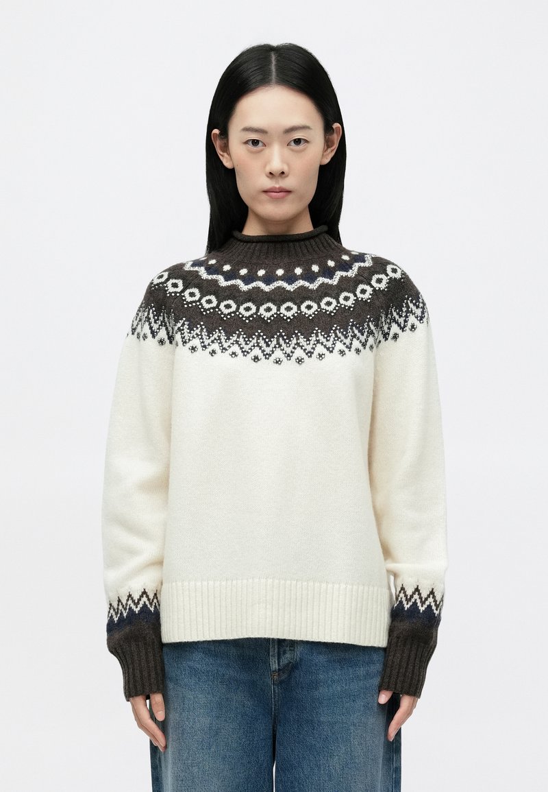 Cremefarvet strikket sweater med en brun mønstret bærestykke, ribbede manchetter og kant. Har geometriske designs i mørkeblå og hvid.