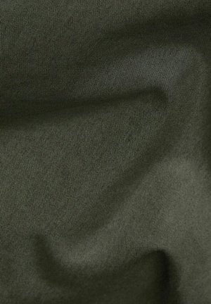 Donkergroene stof met fijne textuur en subtiele plooien die zachte schaduwen en highlights creëren.