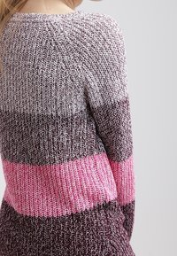 Strickpullover mit einer Farbabstufung von Dunkellila bis Hellrosa. Die Textur ist grob und hat gerippte Akzente im pinken Streifen.