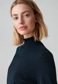 Marineblauwe gebreide coltrui met een geschulpte zoom aan de kraag; een gladde textuur en een aansluitend ontwerp, gedeeltelijk getoond op een model.