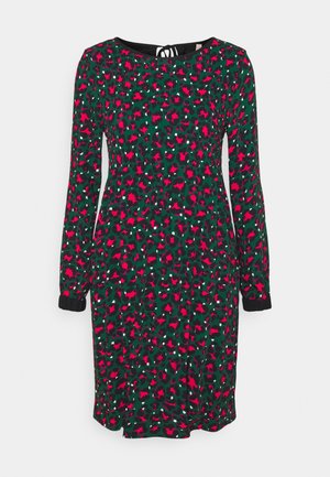 Langärmliges Kleid aus leichtem Stoff, mit grünem Hintergrund und roten sowie weißen abstrakten Mustern. Schwarze Manschettenakzente und eine Bindeschleife am Rücken.