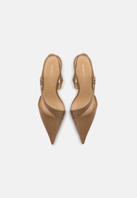 Talons slingbacks en cuir tan avec un bout pointu, présentant un design de bride incurvée et un logo doré sur la semelle intérieure.