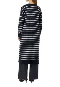 Navy gestreifter Cardigan mit langen Ärmeln und seitlichen Schlitzen, der weiße horizontale Streifen hat. Kombiniert mit dunklen, weit geschnittenen Hosen und Schuhen mit Absätzen.