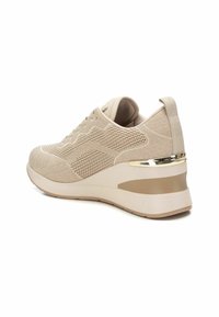 Zapatilla atlética beige con parte superior de punto transpirable, diseño texturizado, suela acolchada y un acento metálico dorado en el talón.