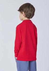 Polo shirt rosso a maniche lunghe con colletto, mostrato da dietro. Tessuto morbido, vestibilità regolare, abbinato a pantaloni blu.
