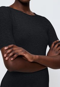 T-shirt noir ajusté à manches courtes, avec une texture lisse et un large décolleté. Le tissu semble légèrement chiné.