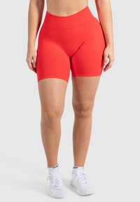 Rode high-waisted sportieve shorts met een gladde textuur, een aansluitend ontwerp en een lengte tot halverwege de dijen. Gepaarde met witte sneakers.