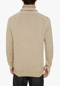 Pull en tricot beige avec un col haut et des manches longues, présentant un motif texturé. Fini avec des poignets et un ourlet côtelés.