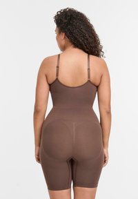 Body shaper marrone con spalline regolabili, texture liscia e lunghezza fino alla metà della coscia, caratterizzato da dettagli di modellatura discreti e una silhouette aderente.