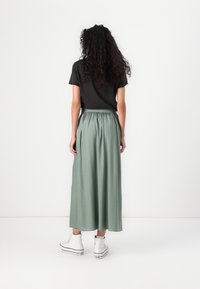 T-shirt nera con maniche corte abbinata a una lunga gonna verde con cintura elastica, completata da sneakers bianche alte.