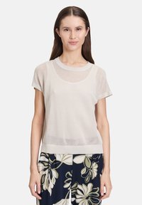 Jasno beżowy sweter z siateczkowego dzianiny, z krótkimi rękawami i okrągłym dekoltem, z miękką, teksturowaną powierzchnią. Połączony z spodniami w kwiatowy wzór.