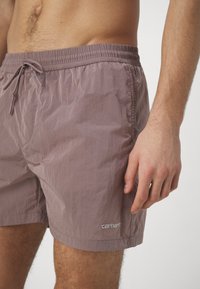 Bañador de hombre en un color malva suave, hecho de material ligero. Cuenta con una cintura elástica con cordón y un bolsillo lateral.