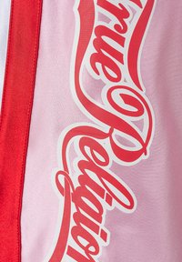 Czerwone logo Coca-Cola na różowej tkaninie z pionowym czerwonym paskiem po lewej stronie.