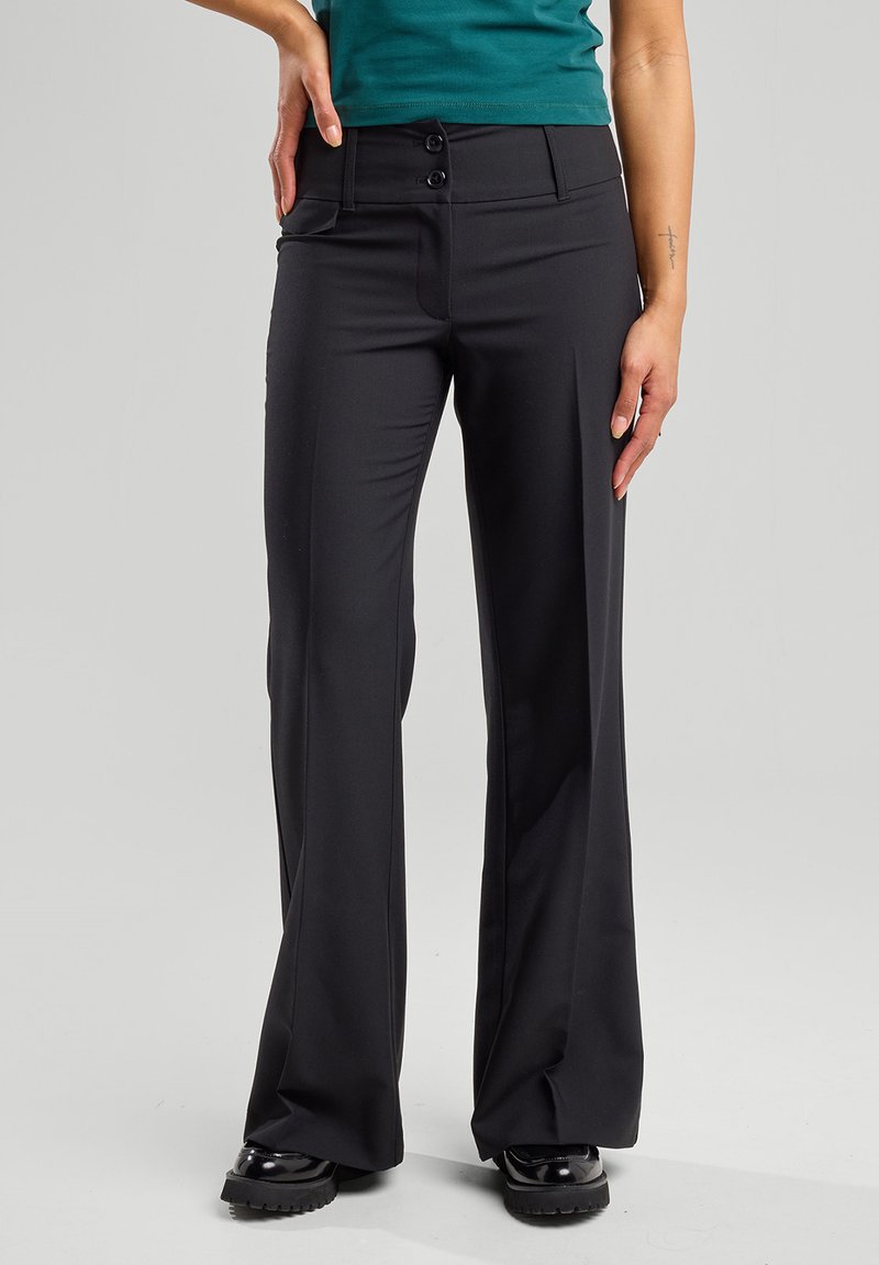 Musta leveälahkeinen housu, jossa on sileä kangastyyli, kaksi etupainiketta, sivutaskut ja istuva vyötärö.