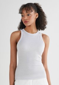 Lichtgrijze geribde tanktop met een ronde halslijn en smalle schouderbandjes. De stof heeft een gladde textuur en een aansluitend ontwerp.