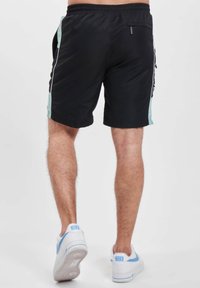 Șorturi atletice negre cu un panou lateral turcoaz, talie elastică și un mic buzunar cu fermoar în spate. Asortate cu adidași albi.
