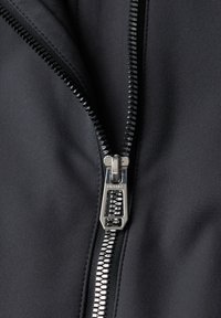 Gros plan d'une veste noire partiellement dézippée avec une fermeture éclair en métal argenté et un curseur marqué "STREET ONE".