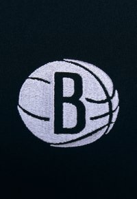 Tela negra con un diseño de baloncesto bordado y una letra "B" central en blanco. El diseño incluye líneas curvas que representan las costuras.