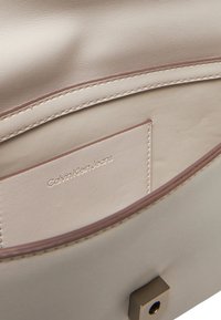 Interno di una borsa a tracolla in pelle beige con texture liscia, dotato di una piccola tasca per carte e il marchio impresso "Calvin Klein Jeans".