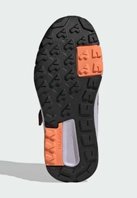 Suela negra con profundas estrías, con acentos en naranja y gris claro. Superficies texturizadas y patrones geométricos que mejoran la sujeción.