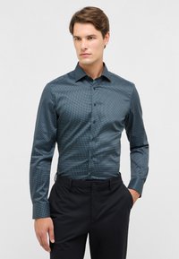 Donkerblauwe button-up shirt met een klein wit stippenpatroon, lange mouwen en een spitse kraag. Draagt met zwarte broeken. Gladde textuur.