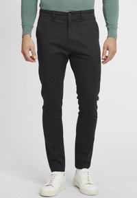 Zwarte katoenen chinos met een slim fit, voorzien van een knoopsluiting, zijzakken en een gladde textuur. Gecombineerd met witte sneakers.