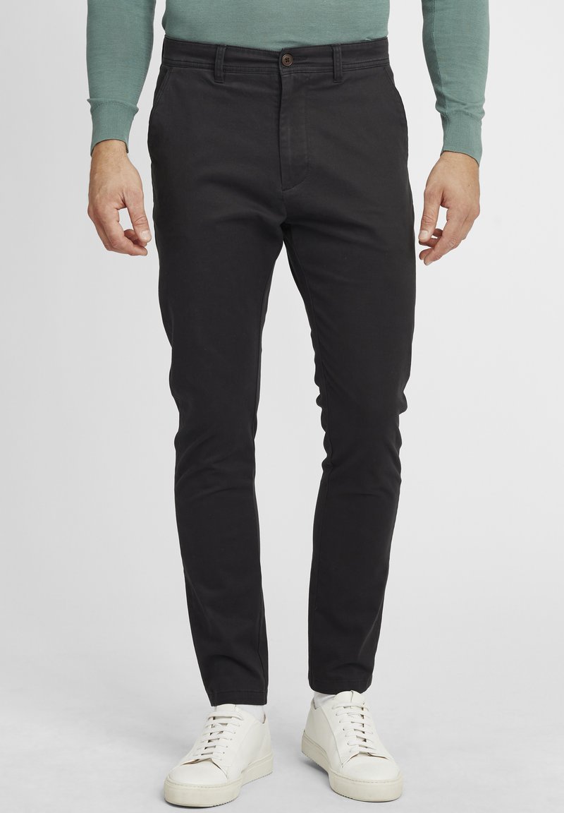 Zwarte katoenen chinos met een slim fit, voorzien van een knoopsluiting, zijzakken en een gladde textuur. Gecombineerd met witte sneakers.