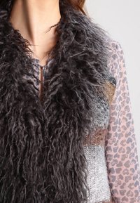 Gilet in pelliccia sintetica di colore grigio scuro con una trama lunga e riccia. Design a strati con zone di argento, marrone e grigio. Aspetto leggero e shaggy.