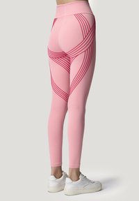 Leggings rosa con strisce curve rosse, vita alta e texture liscia. Abbinati a scarpe da ginnastica bianche, con un design aderente.