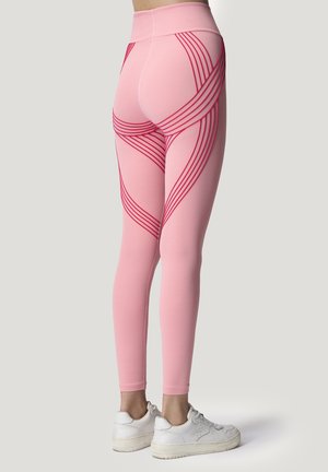 Rosa Leggings mit roten, geschwungenen Streifen, hohem Bund und glatter Textur. Kombiniert mit weißen Sneakers, zeigt ein figurbetontes Design.