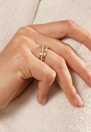 Goldfarbene Ringset bestehend aus zwei miteinander verbundenen Bändern: eines schlicht und das andere mit kleinen klaren Edelsteinen verziert. Glatte Oberfläche, elegantes Design.