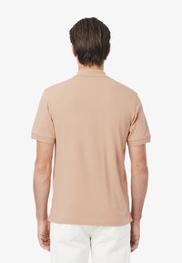 Ljusrosa polo med mjuk yta, korta ärmar och krage, med en enkel design utan mönster eller detaljer.