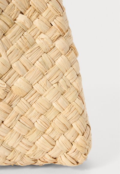 Woven straw bag in light beige. Features a textured, crisscross pattern with a smooth finish. Soft and flexible material.