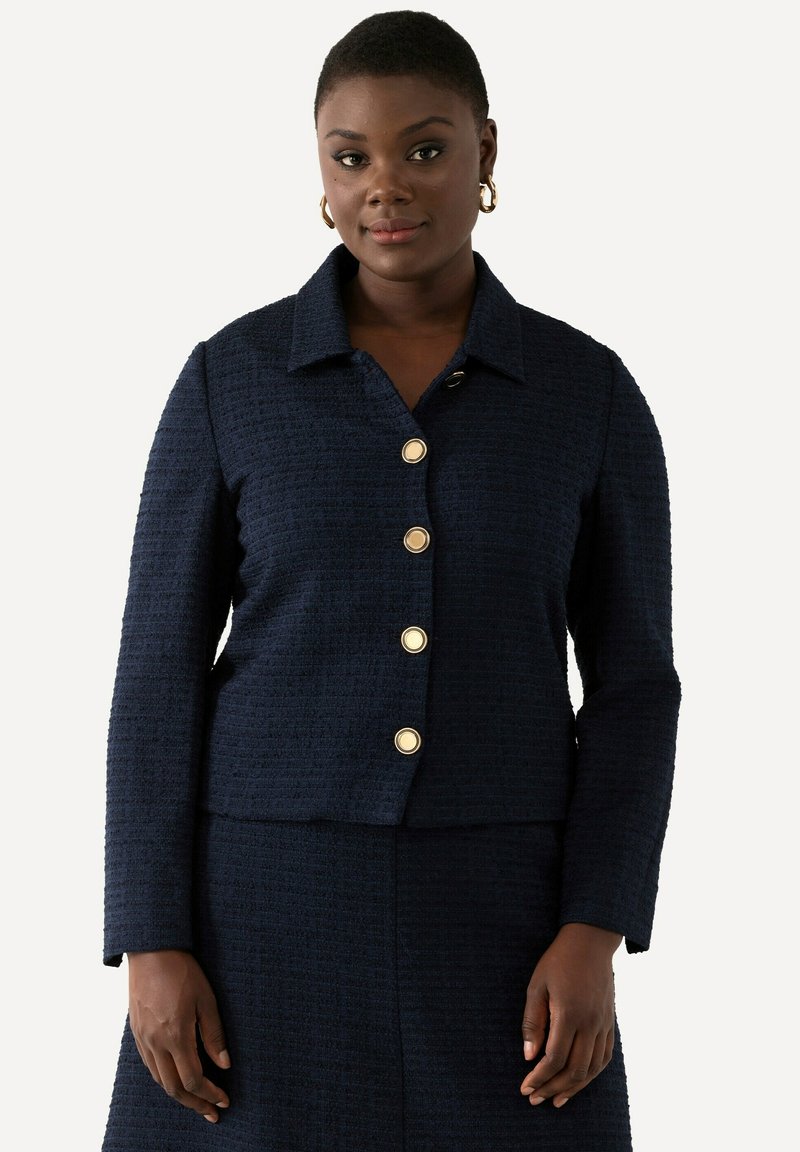 Giacca blu navy con texture e colletto, con sei bottoni dorati sul davanti. Maniche lunghe e vestibilità aderente.