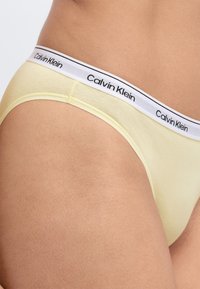 Κίτρινα βαμβακερά εσώρουχα Calvin Klein με λευκή και μαύρη λωρίδα μέσης με λογότυπο. Λείο ύφασμα, χαμηλή μέση, με ελάχιστες ραφές.