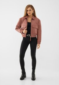 Giacca in finta pelle rosa con colletto, due tasche frontali e polsini a coste, abbinata a jeans skinny neri e stivaletti.