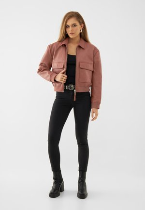 Roze leren look jack met een kraag, twee voorzakken en geribbelde manchetten, gecombineerd met zwarte skinny jeans en enkellaarsjes.