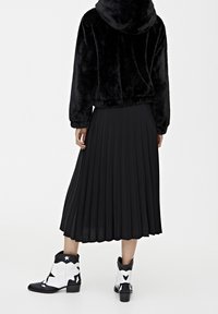 Black faux fur hoodie with a cropped design, paired with a long black pleated skirt and white and black star-patterned ankle boots.