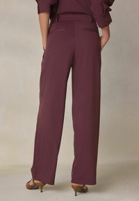 Vinrøde bukser med vide ben og en glat tekstur, med baglommer og en skræddersyet talje, kombineret med brune spidse hæle.