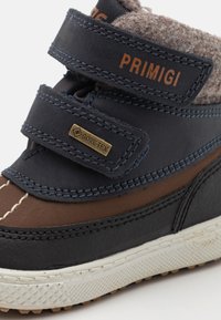 Blå og brune barneboots med borrelåser, myk stoffforing og en teksturert gummisåle. Har en GORE-TEX-etikett.