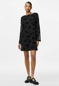 Zwarte jurk met doorschijnende lange mouwen, bloemenvelours patroon, boot neckline, en een ontspannen pasvorm, gecombineerd met zwarte platform schoenen.