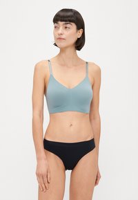 Helles blaues, nahtloses Bustier mit dünnen Trägern und V-Ausschnitt, kombiniert mit schwarzen, minimalistischen Bikinihöschen. Glatte Textur, figurbetonte Form.