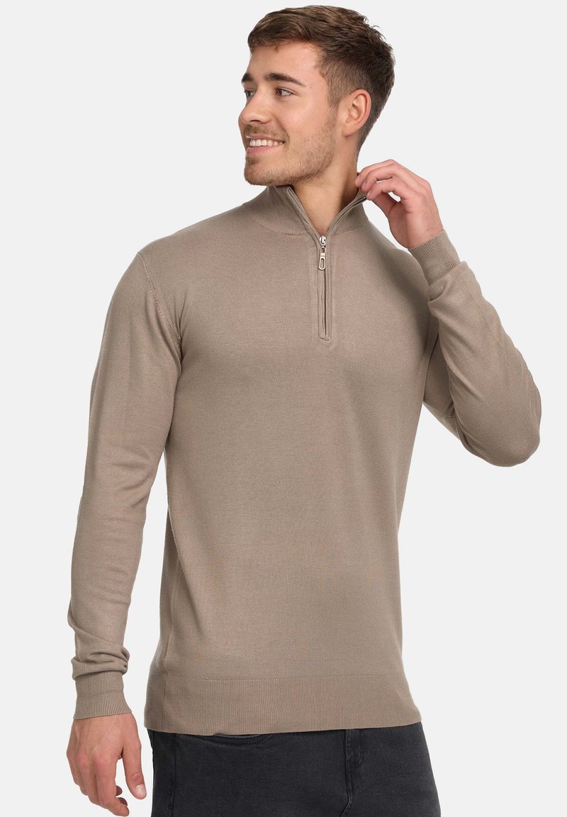 Pull beige à col zippé avec manches longues, poignets côtelés et texture lisse. La fermeture éclair est de ton argenté, ce qui rehausse le design.