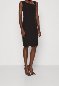Schwarzes ärmelloses Kleid mit strukturiertem Design, diagonalem Ausschnitt und goldfarbenen Akzenten. Glatter Stoff und figurbetonte Silhouette.