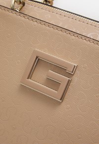 Beige struktureret håndtaske med et præget mønster og et fremtrædende metal G-formet logo. Lynlås lukning med guld accenter.