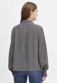 Camicia a righe bianca e nera con colletto, maniche lunghe e polsini con bottoni, caratterizzata da una vestibilità ampia e un design con piega sul retro.