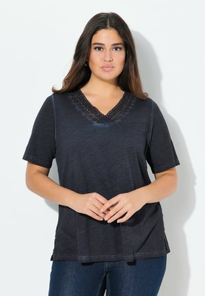 Zwarte T-shirt met korte mouwen en een V-hals, voorzien van kanten details bij de hals en een zachte textuur, gedragen met spijkerbroeken.