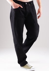 Schwarze Denim-Jeans mit lockerer Passform. Verfügt über fünf Taschen, kupferne Nieten und einen Knopfverschluss. Kombiniert mit grünen Canvas-Sneakern.