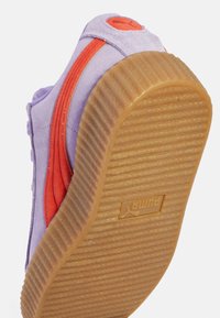 Puma teniska s fialovým semišovým svrškem, oranžovými akcenty, texturovanou gumovou podrážkou a výrazným logem na patě.