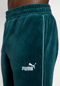 Turkusowe dresy z weluru z elastycznym pasem, z białymi lamówkami po bokach oraz białym logo Pumy z przodu.